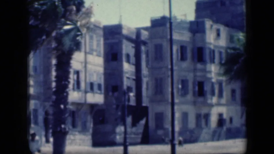 1946 Cairo street view with pale apartment facades, palm trees, and dark street poles in a faded 8mm frame.