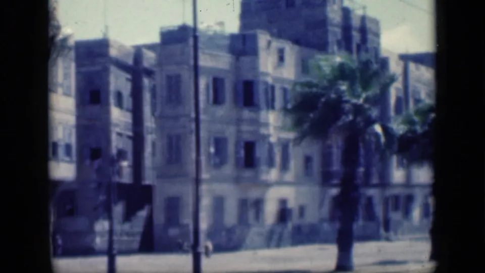 1946 Cairo street scene with apartment buildings, palm fronds, poles, and bright pavement captured on faded 8mm film.