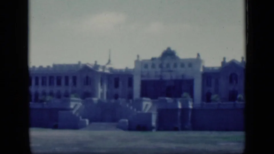 1946 Cairo 8mm frame of a grand pale facade with arched central detail, side wing, low wall, and blue-shifted film color.