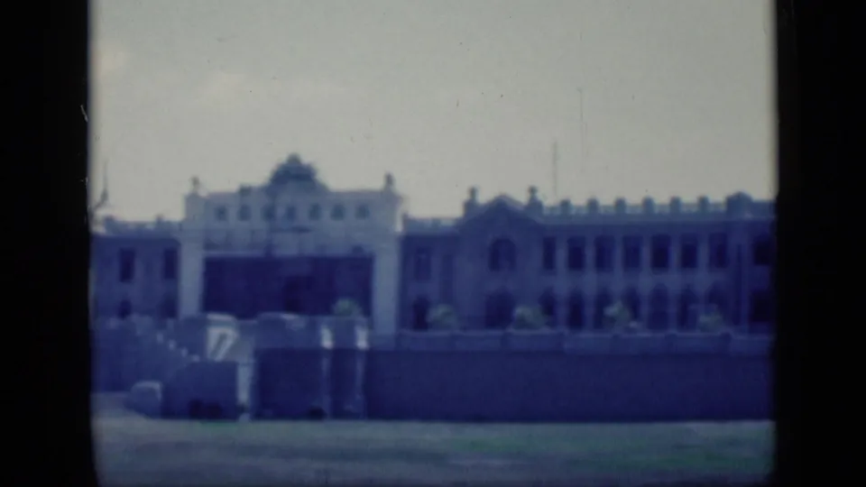 1946 Cairo home-movie still showing the camera panning along a grand building exterior with repeated windows, arched bays, and terrace-like walls.
