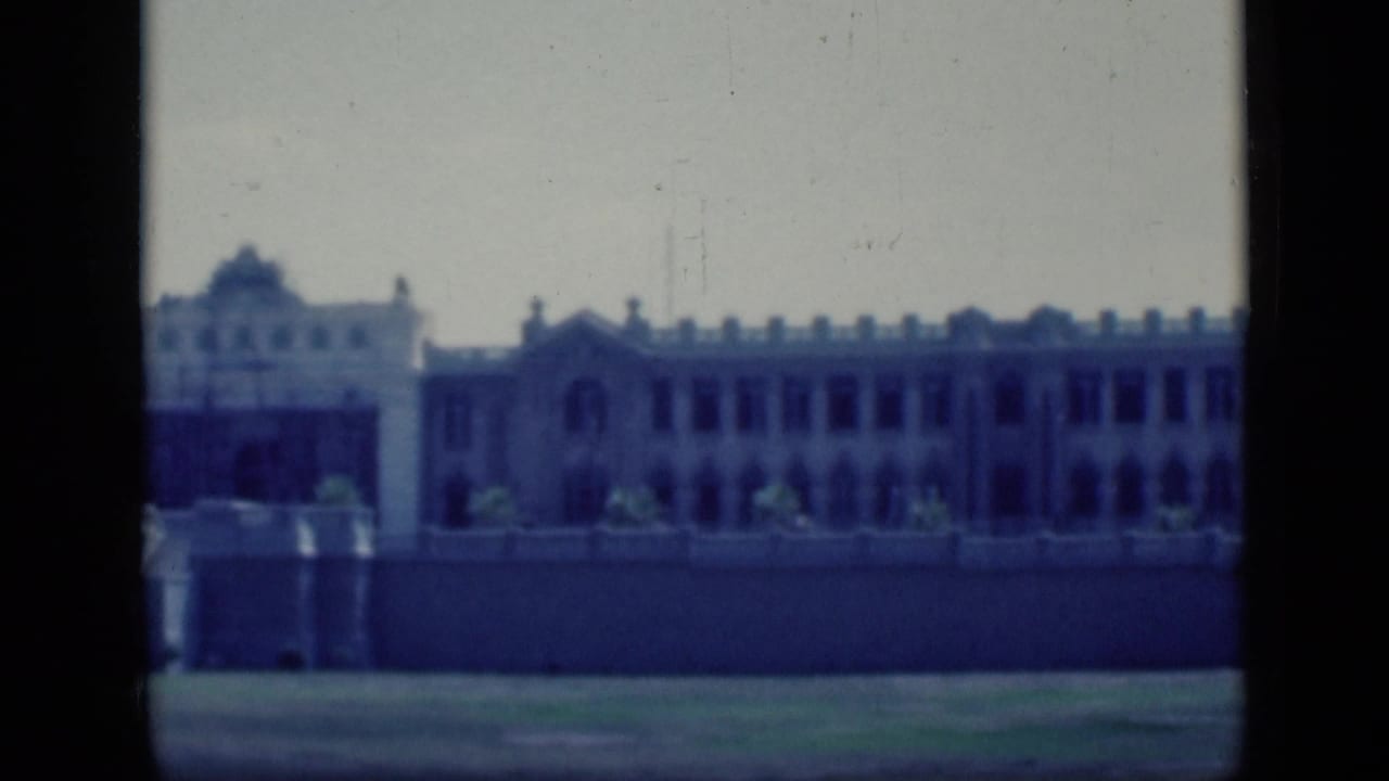 1946 Cairo 8mm frame showing a distant pale building with arched openings, low wall, grass foreground and dark film borders.