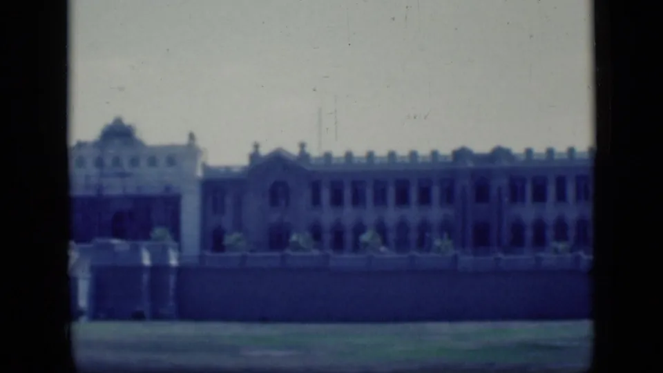 1946 Cairo 8mm frame showing a distant pale building with arched openings, low wall, grass foreground and dark film borders.