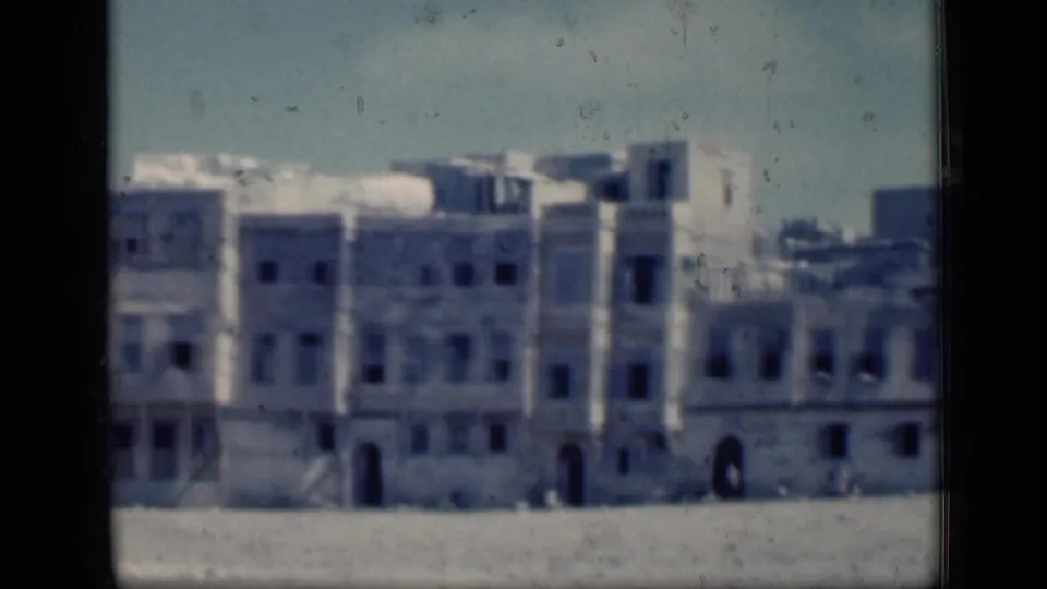 1946 Cairo footage ending on weathered multi-story facades with dark windows, arched entrances, and open ground in front.