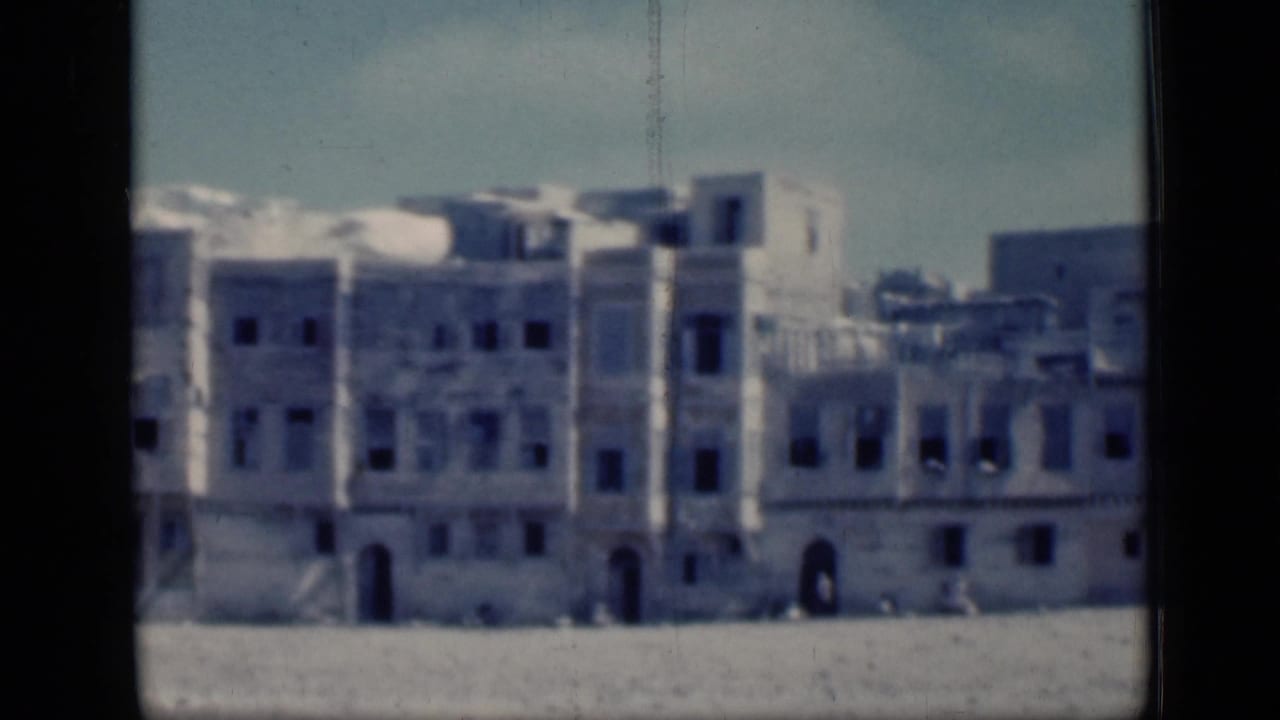 1946 Cairo home-movie frame showing pale historic-looking buildings with arches and dark windows across an open plain.