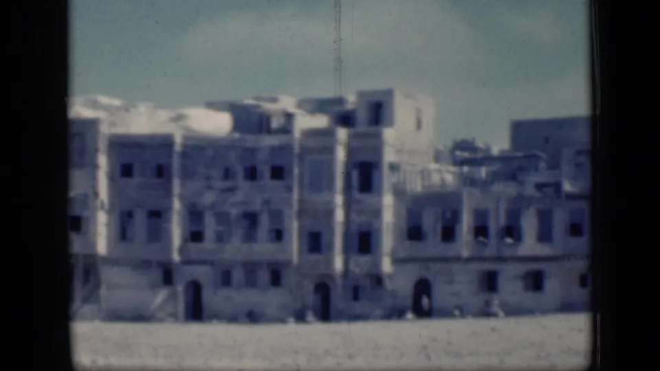 1946 Cairo home-movie frame showing pale historic-looking buildings with arches and dark windows across an open plain.