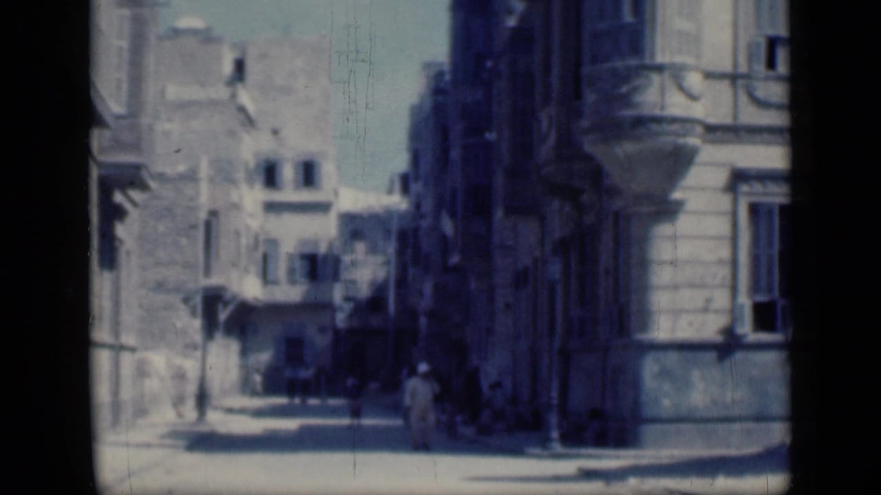 1946 Cairo street corner with tall building facades, balconies, deep shade, and distant pedestrians crossing the frame.