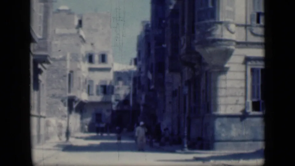1946 Cairo street corner with tall building facades, balconies, deep shade, and distant pedestrians crossing the frame.