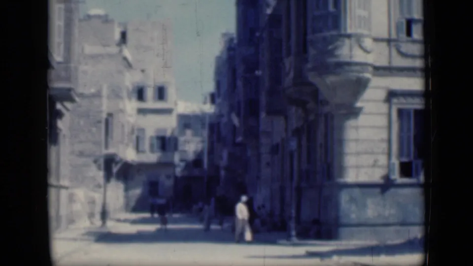 1946 Cairo street scene with pedestrians near a curb, shaded facades, balconies, and a bright open roadway.