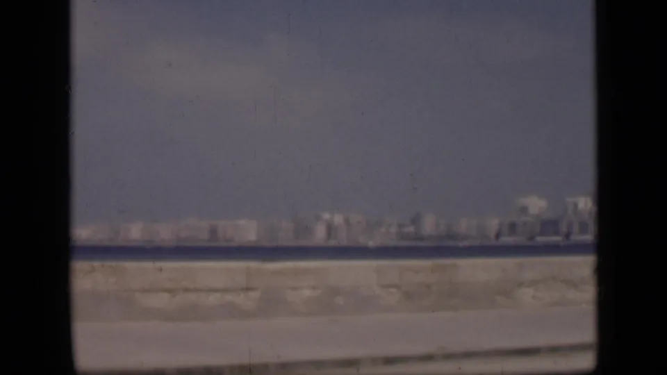1946 Cairo home-movie frame showing a distant cityscape across water, with a hazy sky, pale embankment, and visible 8mm gate borders.