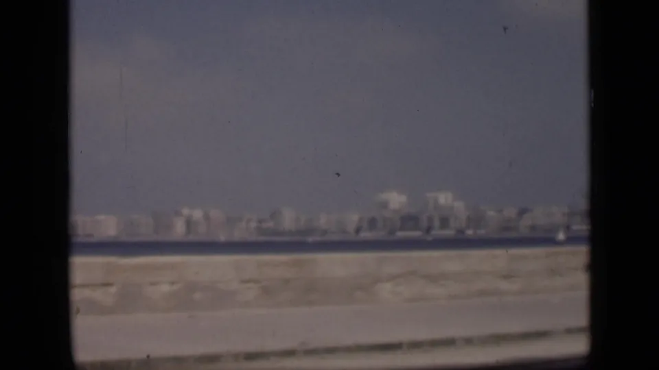 Soft 8mm frame of Cairo identified by metadata, showing a distant waterside skyline, pale foreground edge, and scattered film scratches.