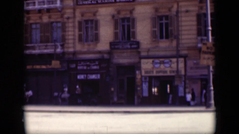 1946 Cairo home-movie frame showing shopfront signage, upper-story windows, pedestrians, and a street-level building entrance.