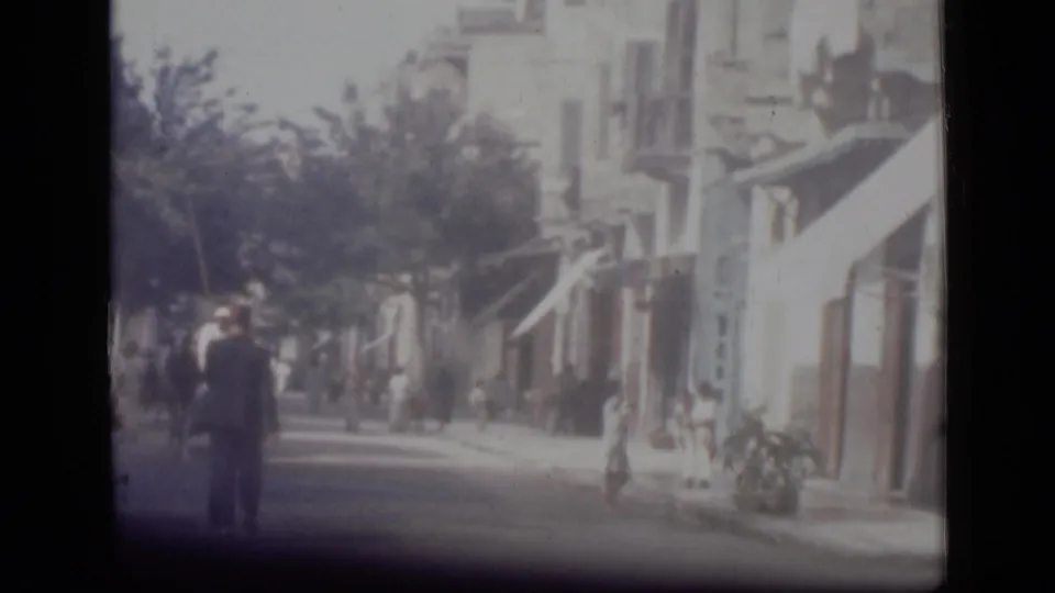 Soft, faded 1946 Cairo street view showing pedestrians, trees, and building fronts from a home-movie perspective.
