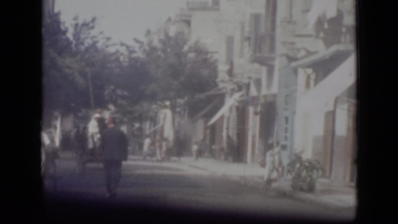 1946 Cairo street view from 8mm footage, showing pedestrians walking past awnings, trees, and sunlit building fronts.