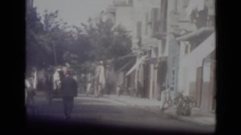 1946 Cairo street view from 8mm footage, showing pedestrians walking past awnings, trees, and sunlit building fronts.