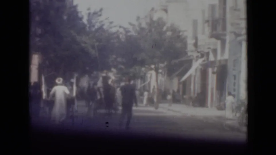 1946 Cairo street scene with a robed pedestrian, other walkers, awnings, trees, and older building facades in soft 8mm color.
