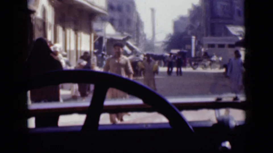1946 Cairo street view from inside or beside a moving vehicle, with pedestrians, storefronts, and a horse-drawn cart in the road.