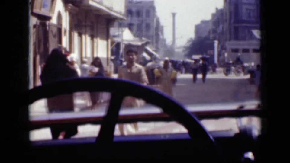 1946 Cairo street view from inside a vehicle, with a large steering wheel, pedestrians, shopfronts, and awnings visible through the windshield.