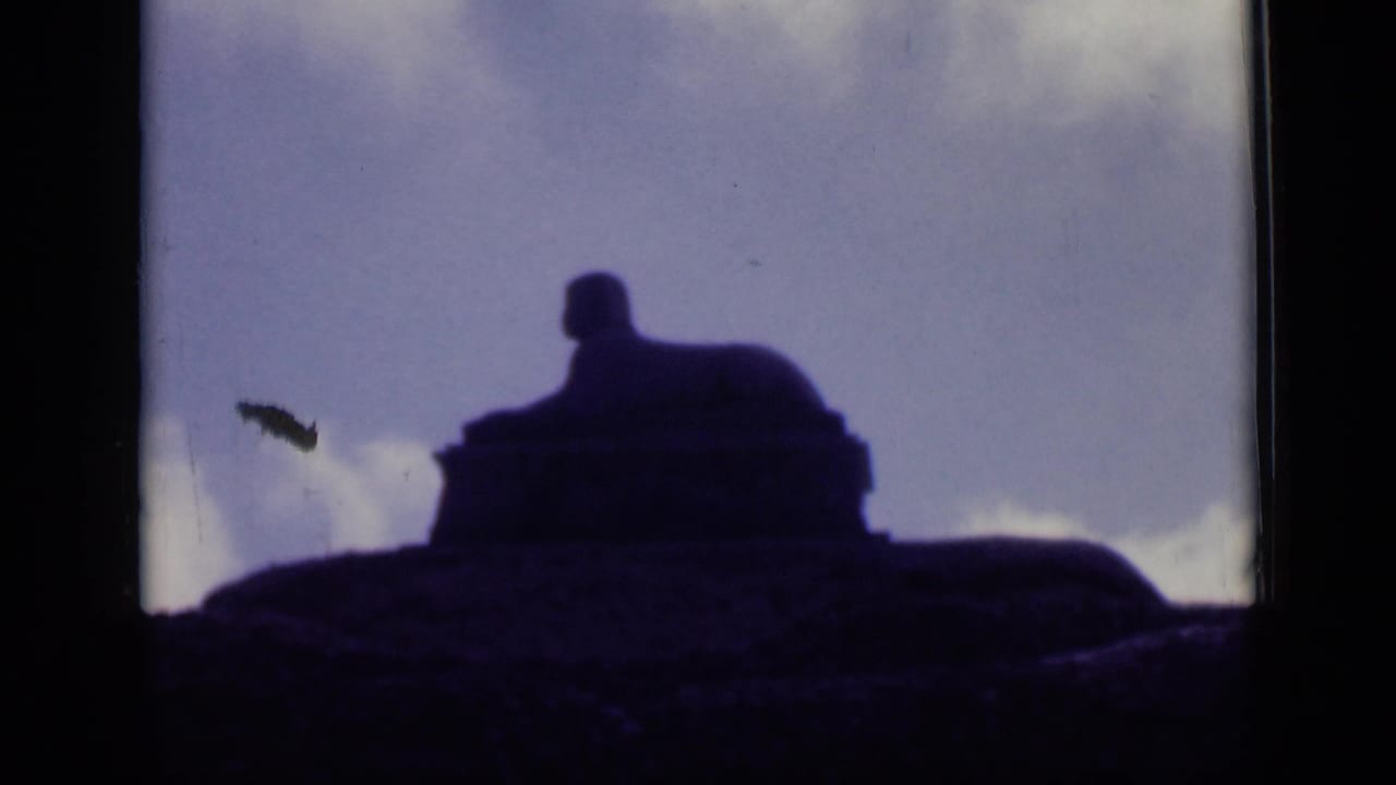 1946 Cairo home-movie frame showing a sphinx-like stone monument in deep silhouette against blue sky and low white clouds.