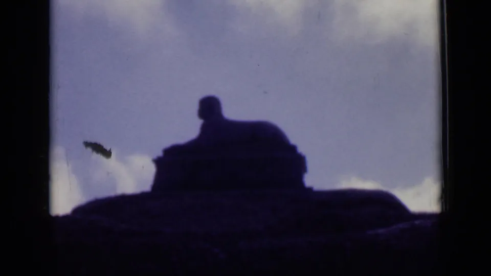 1946 Cairo home-movie frame showing a sphinx-like stone monument in deep silhouette against blue sky and low white clouds.