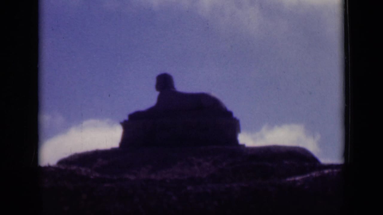 1946 Cairo footage frames the sphinx-like monument as a soft, dark outline rising from rocky ground beneath a washed blue sky.