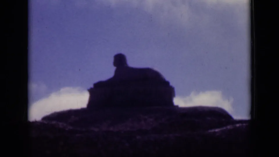 1946 Cairo footage frames the sphinx-like monument as a soft, dark outline rising from rocky ground beneath a washed blue sky.
