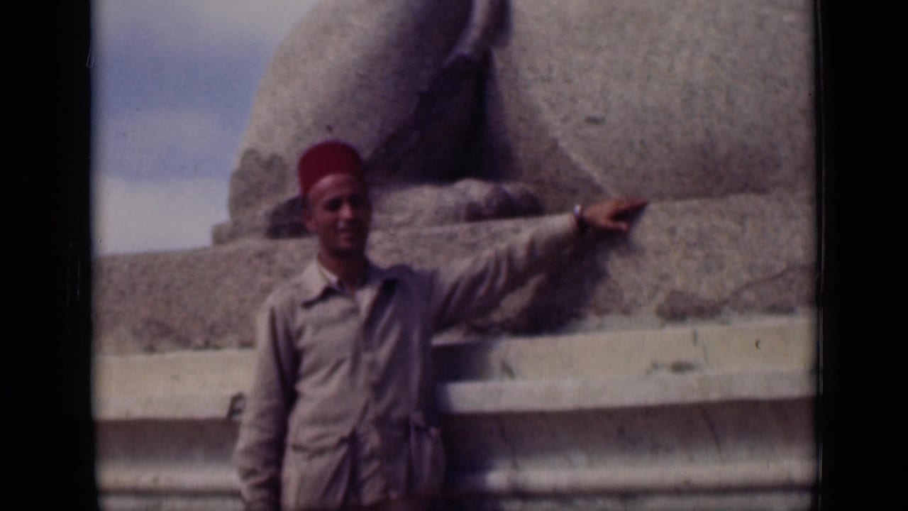 Man in a red fez and tan outfit points while standing near the Sphinx base.