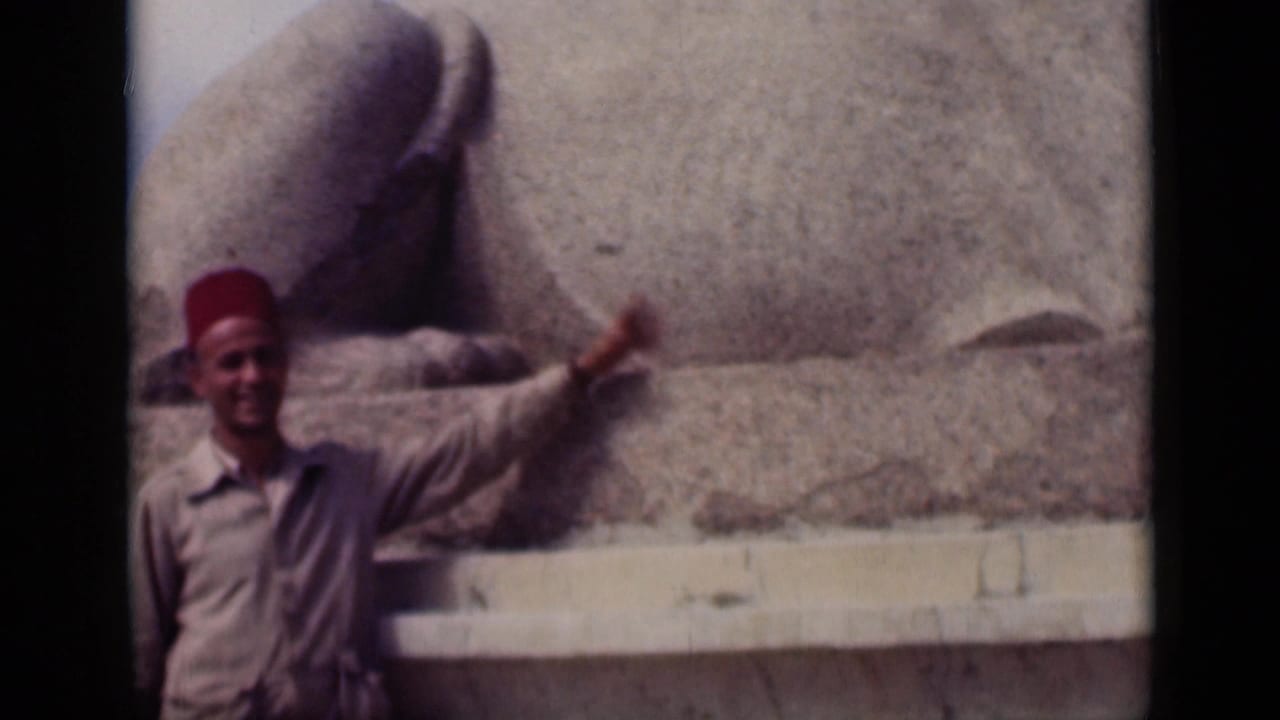 Man in a red fez gestures beside the body of the Great Sphinx.