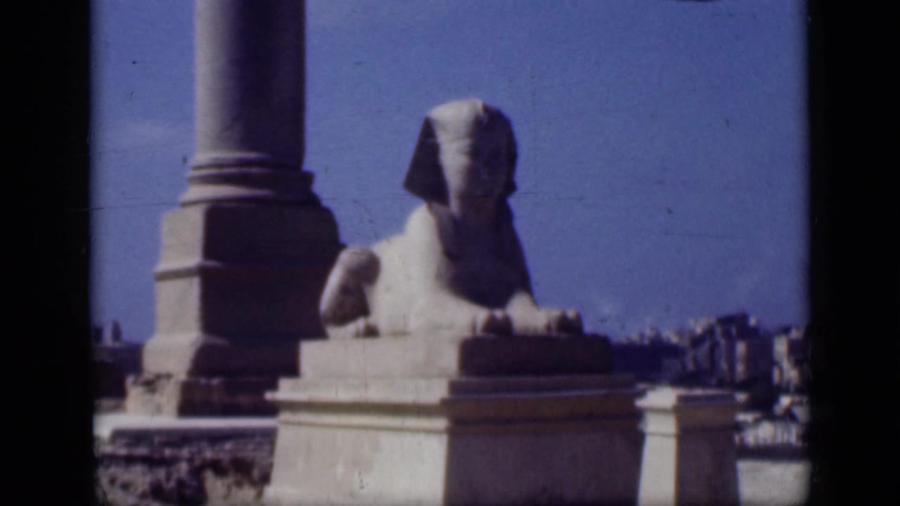1946 Cairo frame showing the Sphinx from farther back, with a nearby column base, pedestal, sky, and small visitor figures.