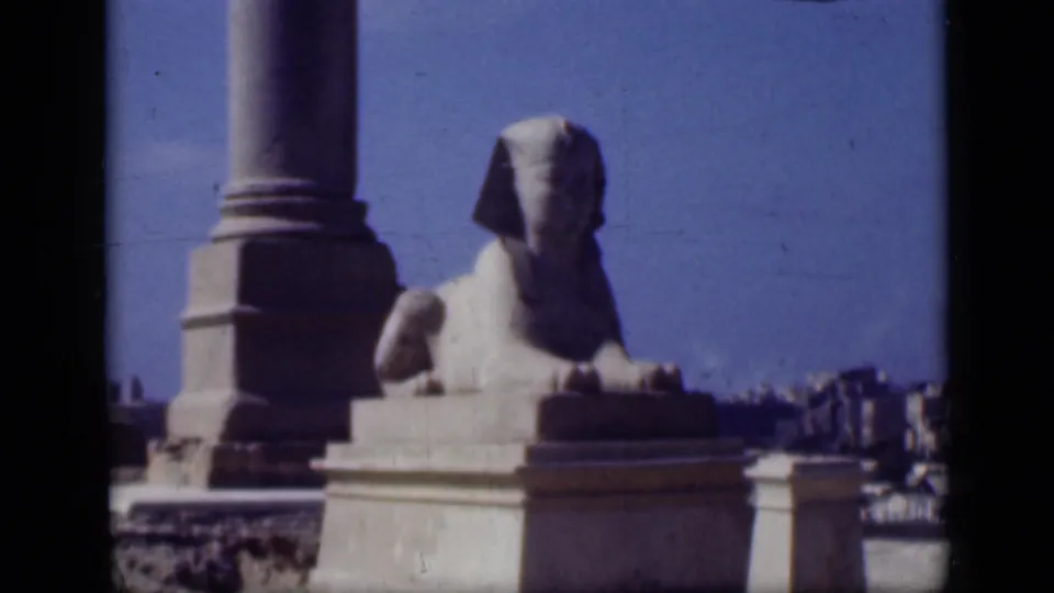 1946 Cairo frame showing the Sphinx from farther back, with a nearby column base, pedestal, sky, and small visitor figures.