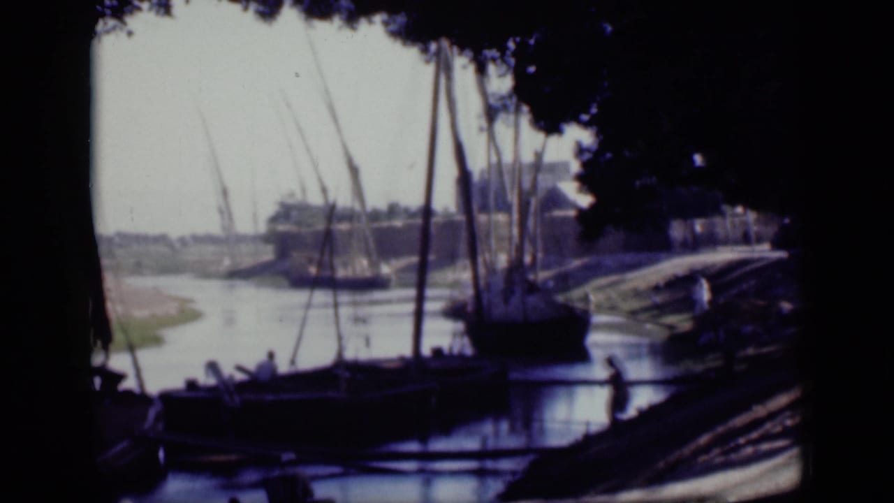 1946 Cairo home-movie frame of several sailboats beside a shaded riverbank, with masts crossing the bright sky.