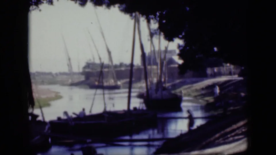 1946 Cairo home-movie frame of several sailboats beside a shaded riverbank, with masts crossing the bright sky.