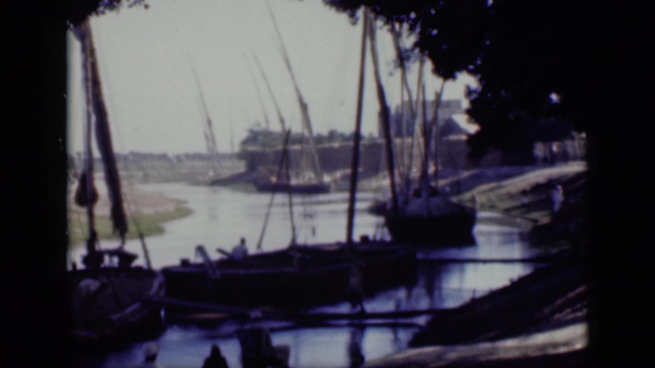 1946 Cairo riverbank frame showing moored sailboats, small figures, tree shade, and distant waterfront buildings.
