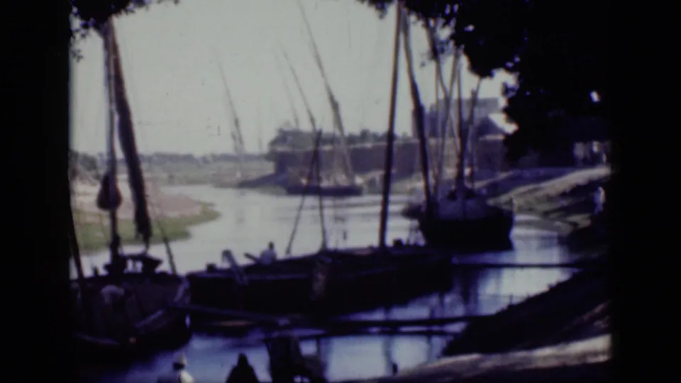 1946 Cairo canal view with docked wooden sailing boats, masts, rigging, shaded foreground trees, and a bright far bank.