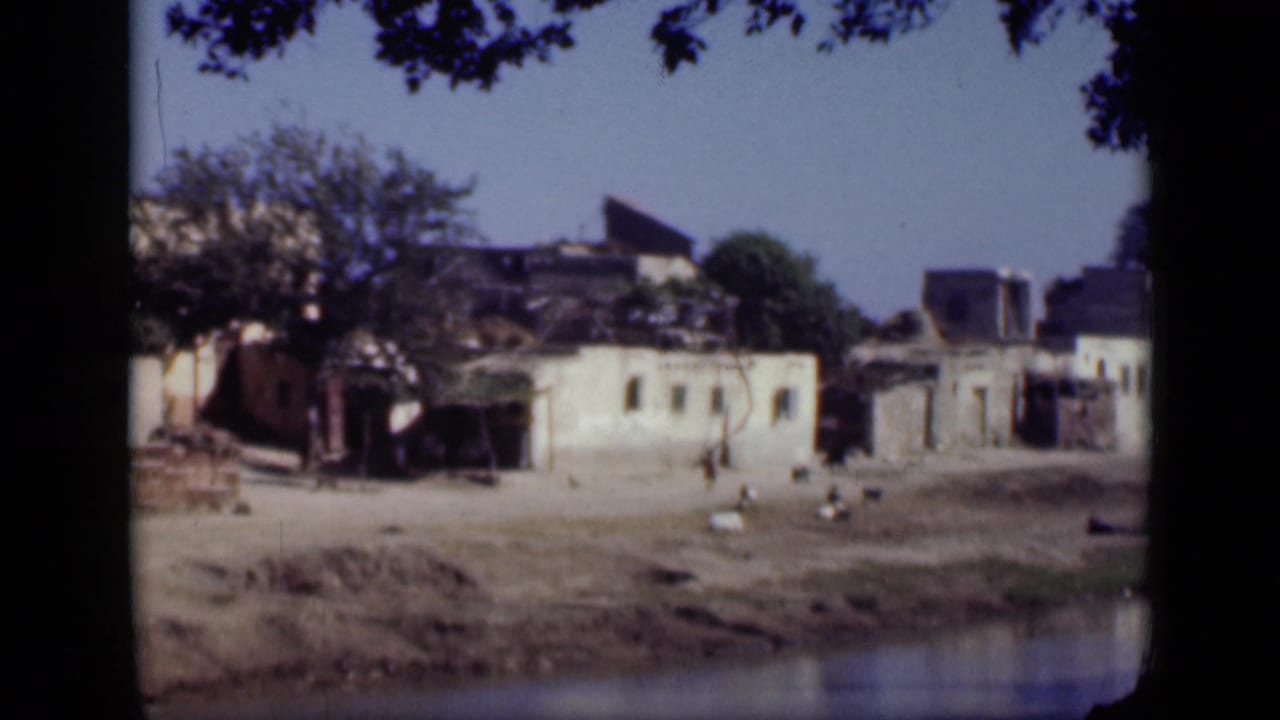Waterfront buildings with damaged walls and a few distant people under tree shade.