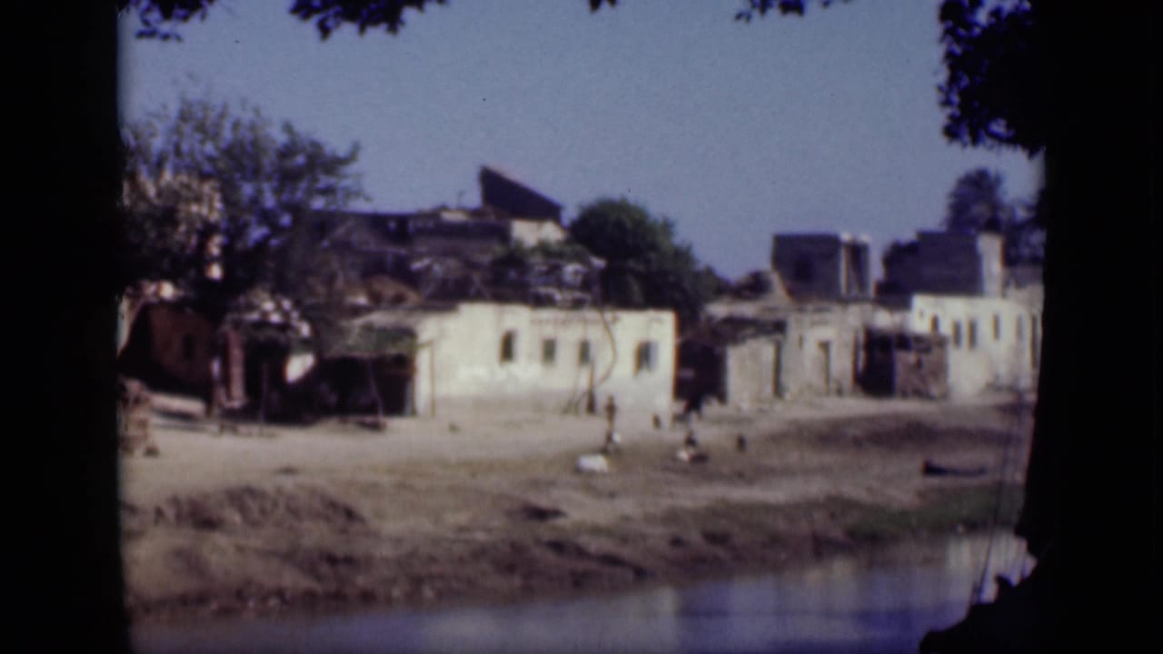 Low waterfront structures, open dusty ground, and small figures near the shore.