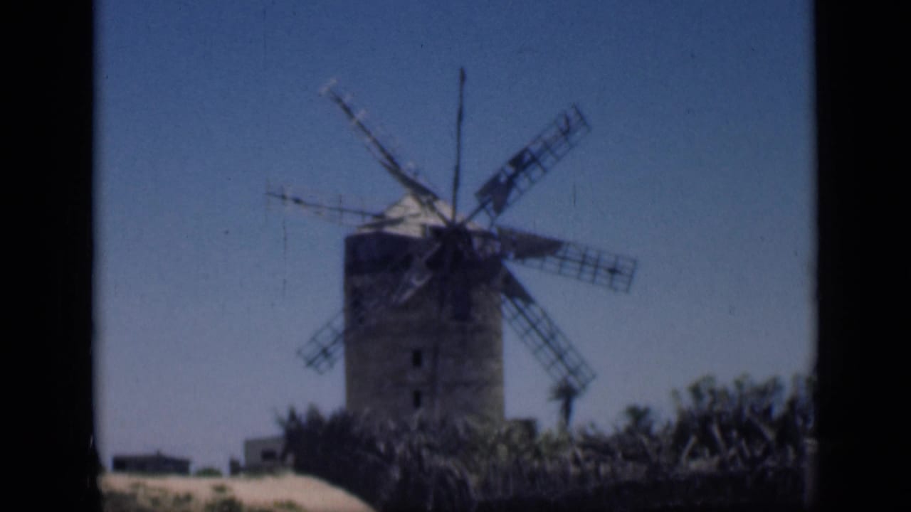 1946 Cairo home-movie frame centered on a weathered windmill, with arid ground and low vegetation at its base.