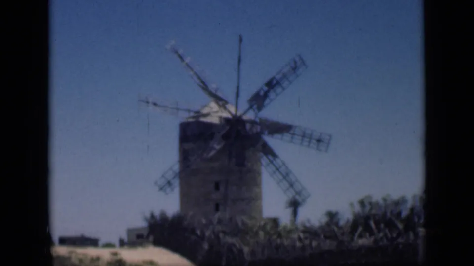 1946 Cairo home-movie frame centered on a weathered windmill, with arid ground and low vegetation at its base.