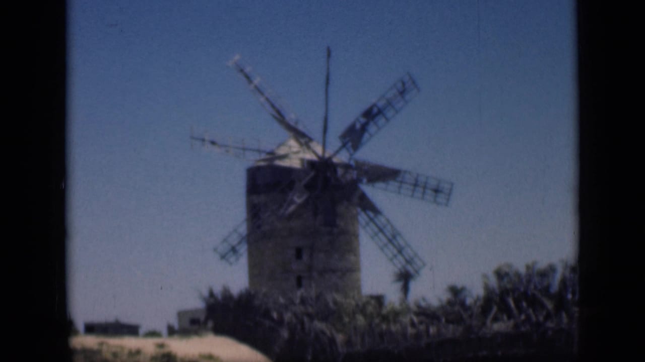 Weathered wooden windmill with lattice blades against a blue sky.