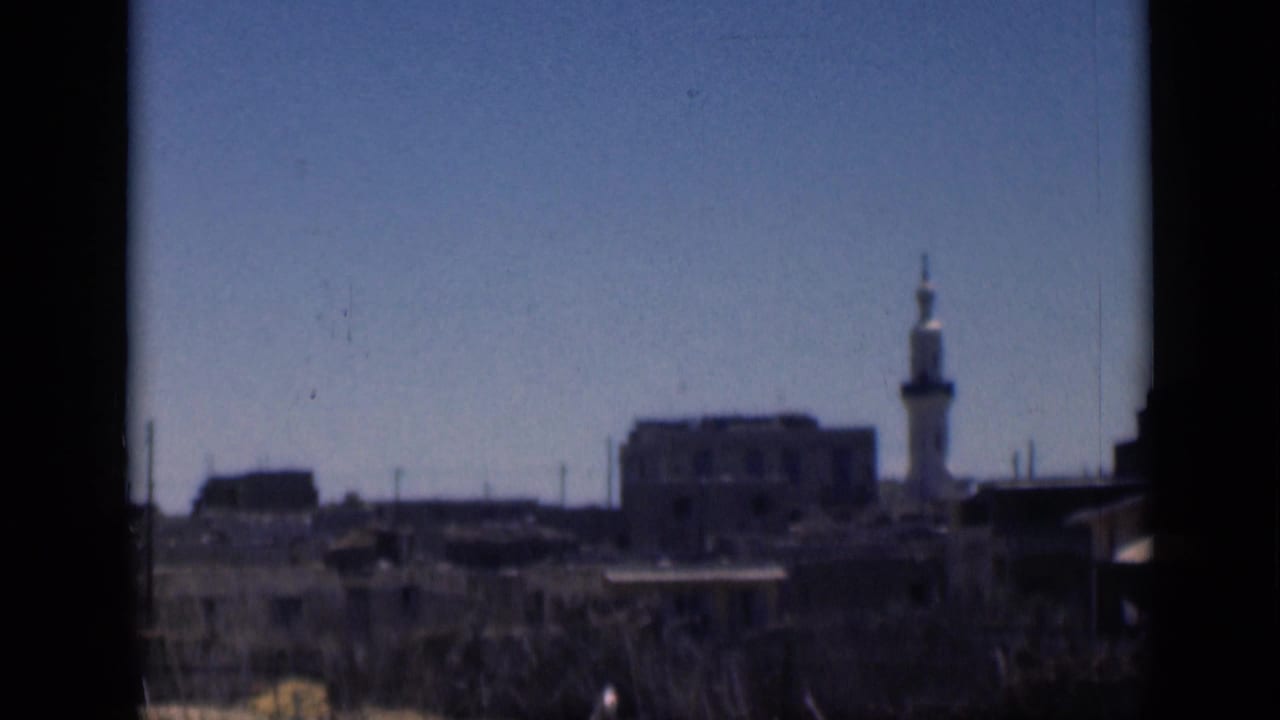 1946 Cairo skyline frame with a white minaret, low buildings, foreground vegetation, and soft 8mm color.
