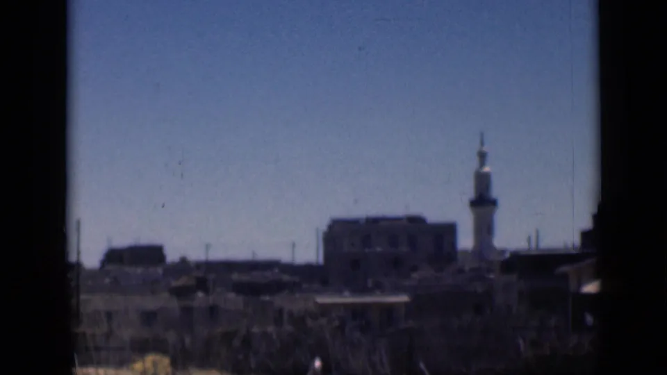 1946 Cairo skyline frame with a white minaret, low buildings, foreground vegetation, and soft 8mm color.