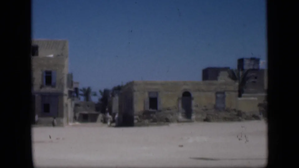 1946 Cairo-area frame with weathered low buildings, shutter-like dark openings, palms, and bright sandy ground seen from a distant home-movie viewpoint.