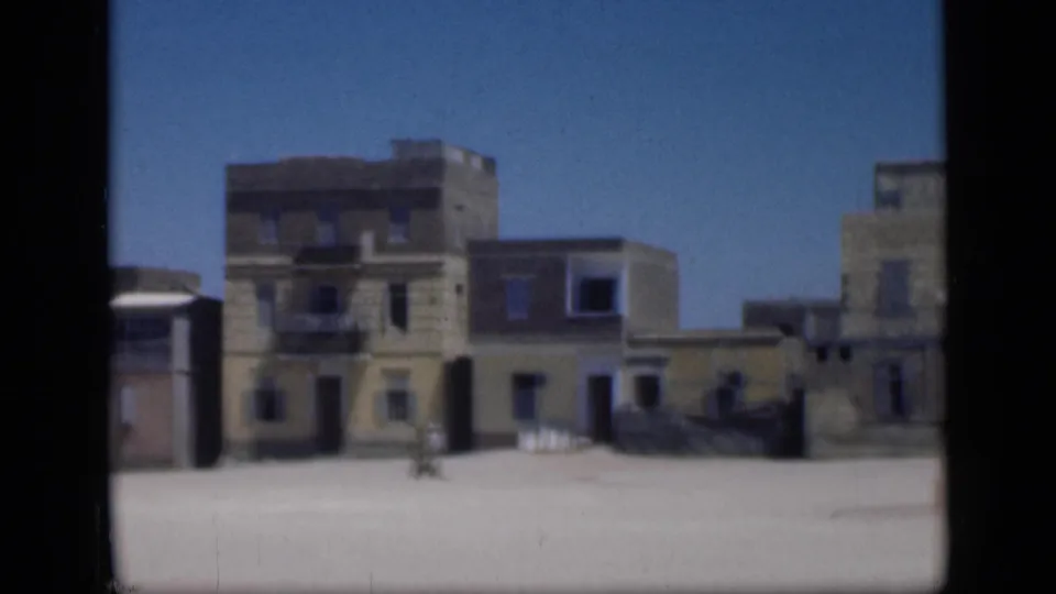 1946 Egypt home-movie frame showing pale masonry buildings and open sandy ground, with soft 8mm focus and dark film borders.
