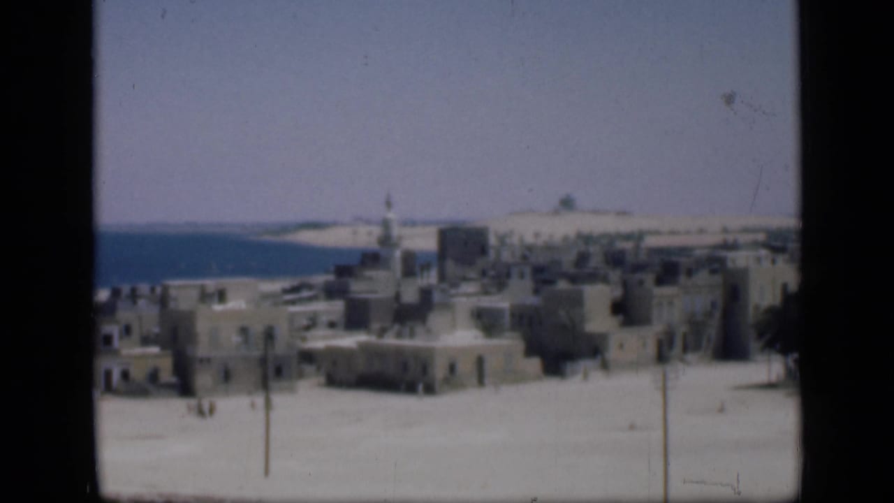 Metadata-supported Cairo, Egypt view with a minaret above low buildings, open sandy foreground, and a blue distant horizon.
