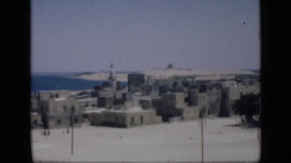 Wide 1946 Egypt cityscape frame with low masonry buildings, a minaret, small distant pedestrians, and faded 8mm color.