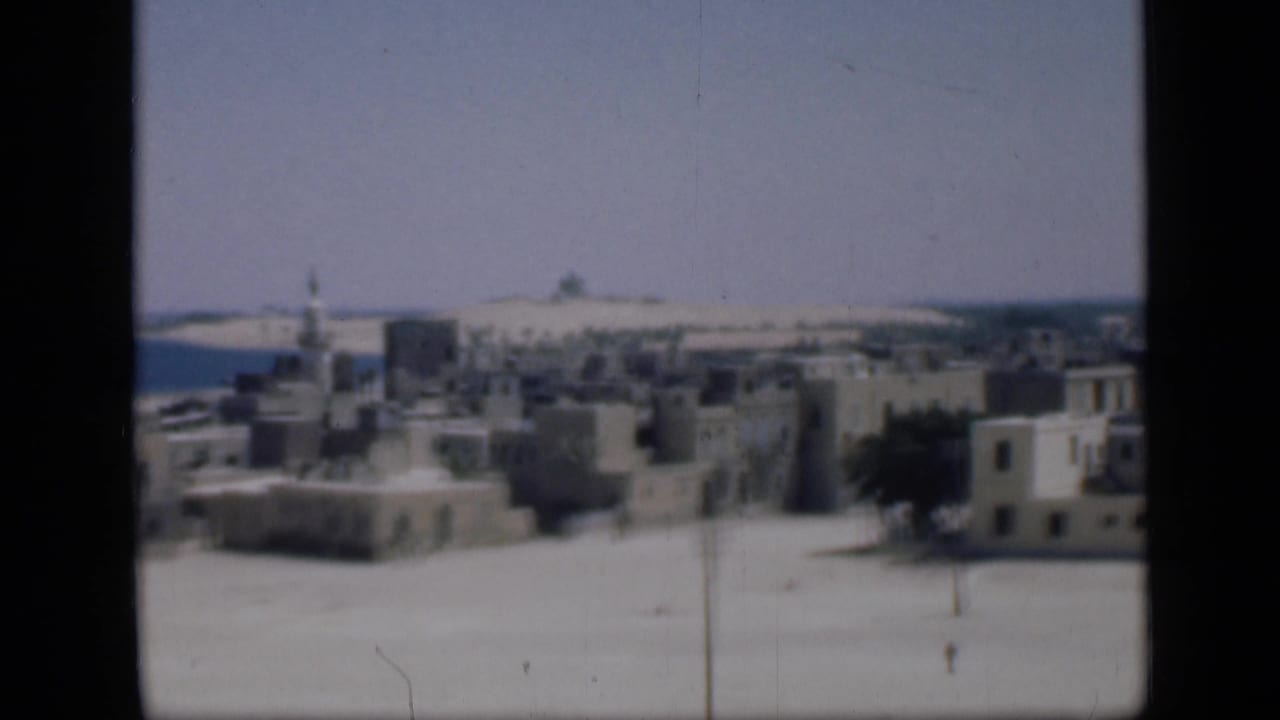 1946 Cairo home-movie view of flat-roofed pale buildings, a minaret, sandy foreground, and distant horizon.