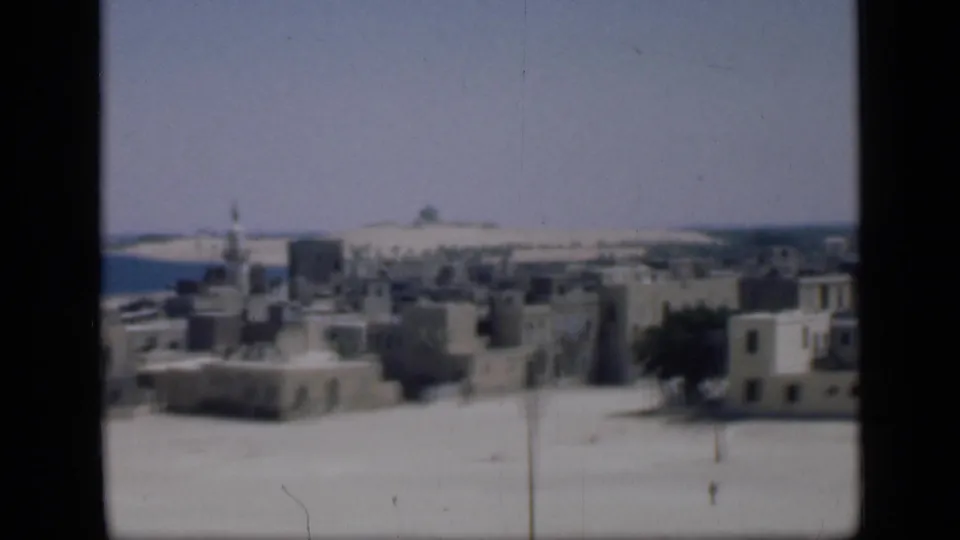 1946 Cairo home-movie view of flat-roofed pale buildings, a minaret, sandy foreground, and distant horizon.