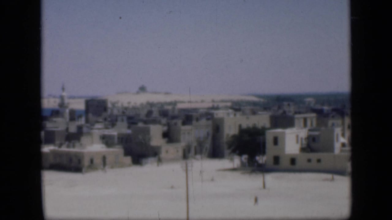 1946 Cairo panorama with low-rise buildings, a minaret at left, sandy foreground, and faint distant water or horizon.