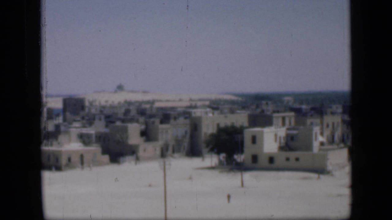 1946 Cairo view with clustered pale buildings, sparse trees, open sandy ground, and small distant pedestrians.