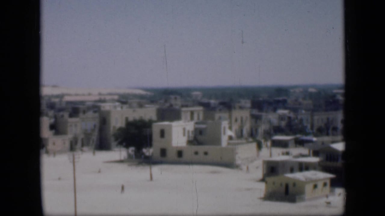 Similar elevated view of pale buildings with flat roofs and open ground.
