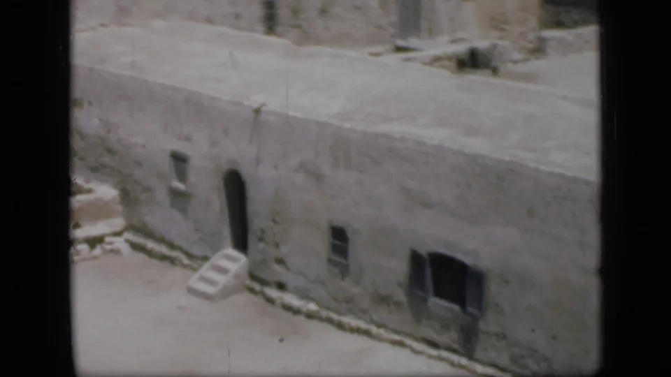 1946 Cairo travel frame showing a weathered flat-roofed building, arched doorway, small windows and sandy exterior space.